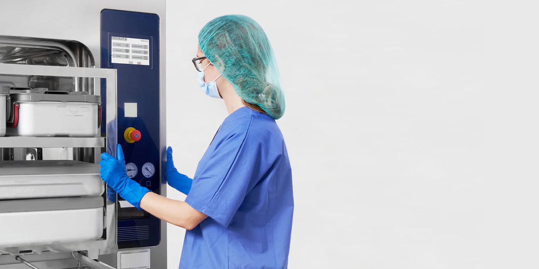 Person in blue scrubs and hairnet operating a medical device in a sterile environment